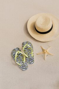 Flatlay of summer travel musthaves including sunglasses, straw hat, sunscreen, beach bag, sandals, and passport cover, perfect for a sunny holiday.